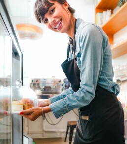 smiling woman with apron holds cakes from showcase